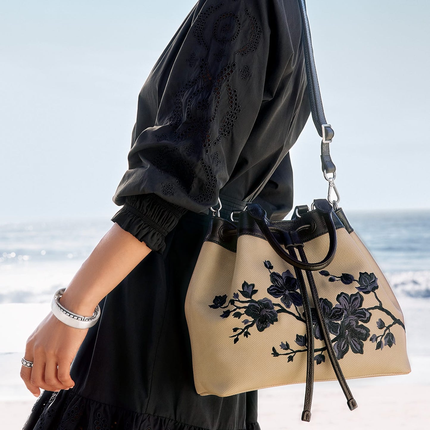 Model with a Brighton beige canvas handbag featuring navy floral embroidery and black leather trim and straps