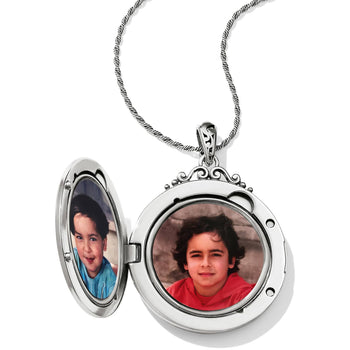 Brighton silver-plated round locket necklace shown open with two photos inside and ornate filigree bail on a white background