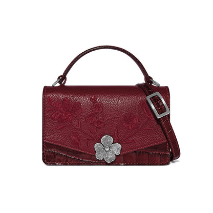Brighton burgundy handbag with floral embroidery, croc-embossed trim, silver-tone flower clasp, and top handle on a white background