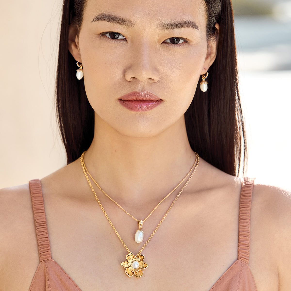 Model wearing Brighton pearl drop earrings paired with layered gold-tone necklaces featuring pearl pendant and floral pendant