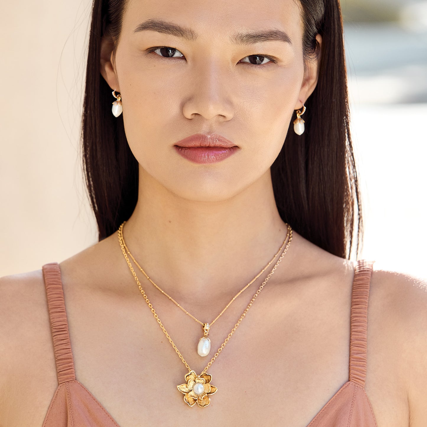 Model wearing Brighton pearl drop earrings paired with layered gold-tone necklaces featuring pearl pendant and floral pendant
