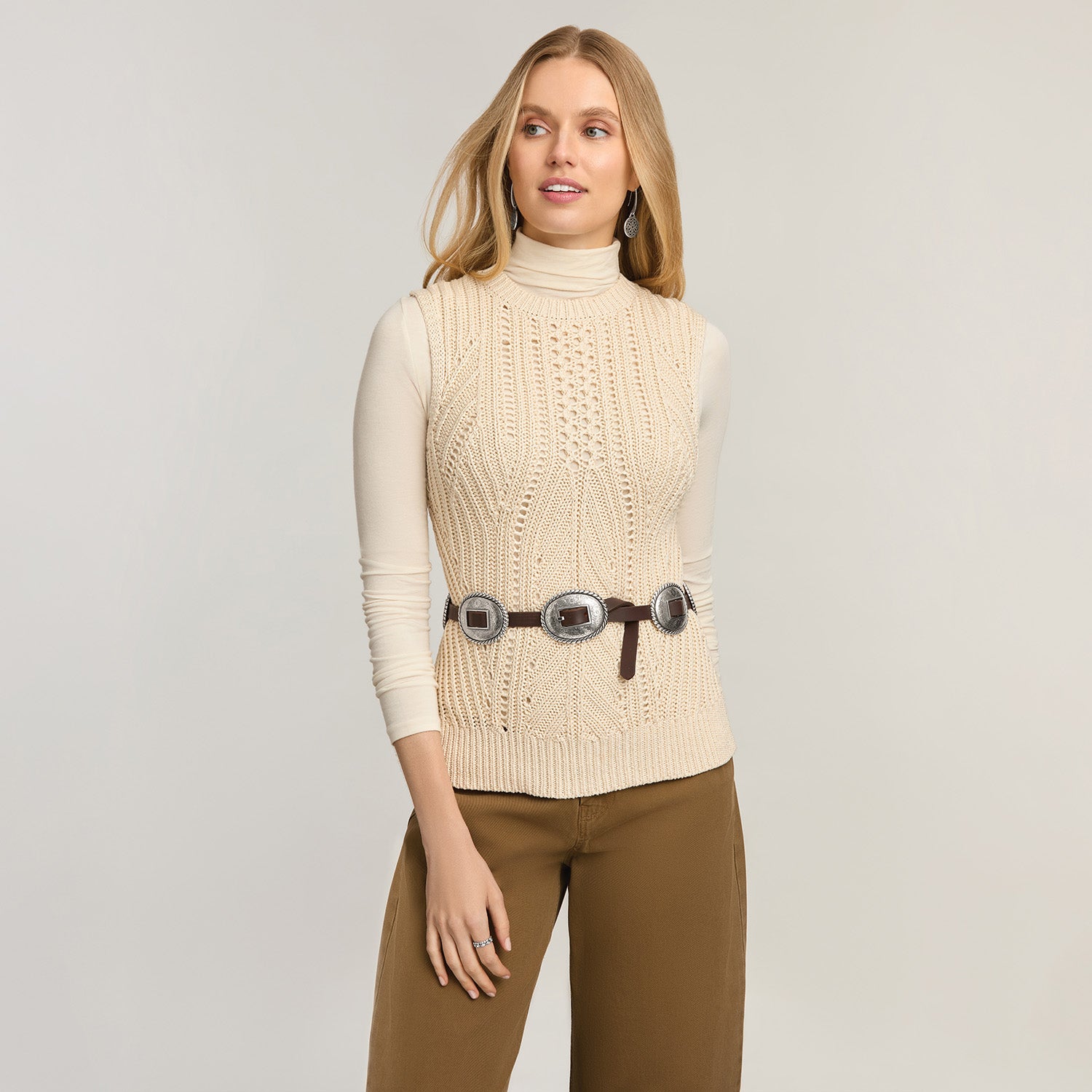 Model wearing a Brighton leather belt with three silver-tone concho medallions over a cream cable-knit top