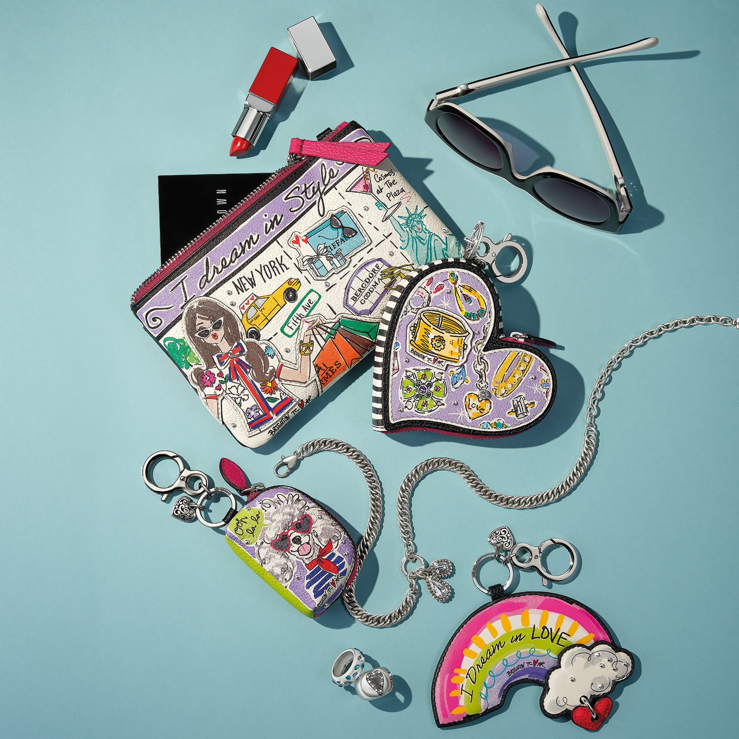 Brighton leather pouch with illustrated New York print, styled with sunglasses and other accessories on blue background