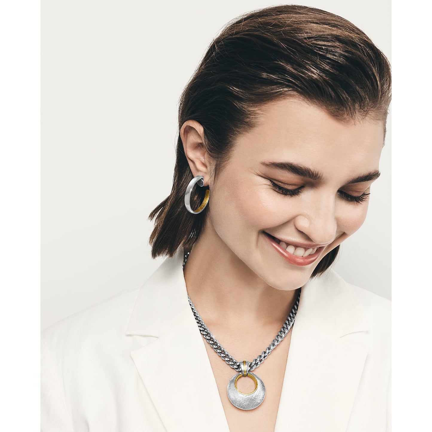 Model wearing Brighton two-tone hoop earrings paired with a silver curb chain necklace and circular two-tone pendant