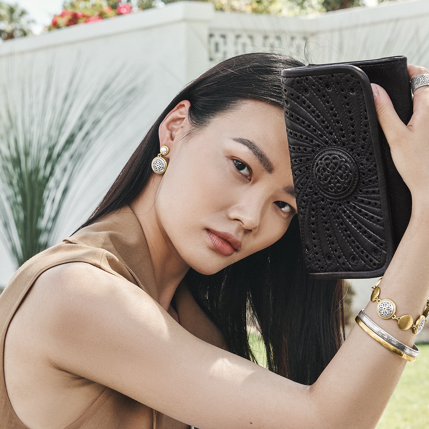 Model wearing Brighton silver and gold drop earrings with coordinating Brighton bracelets and holding a black embossed wallet