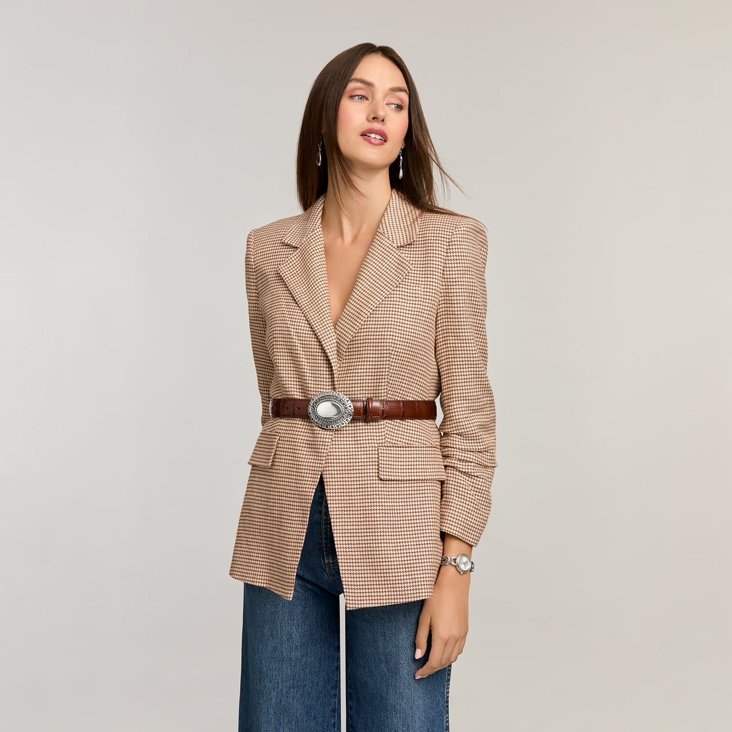 Model wearing a Brighton brown croc-embossed leather belt with ornate silver-tone oval buckle over houndstooth blazer