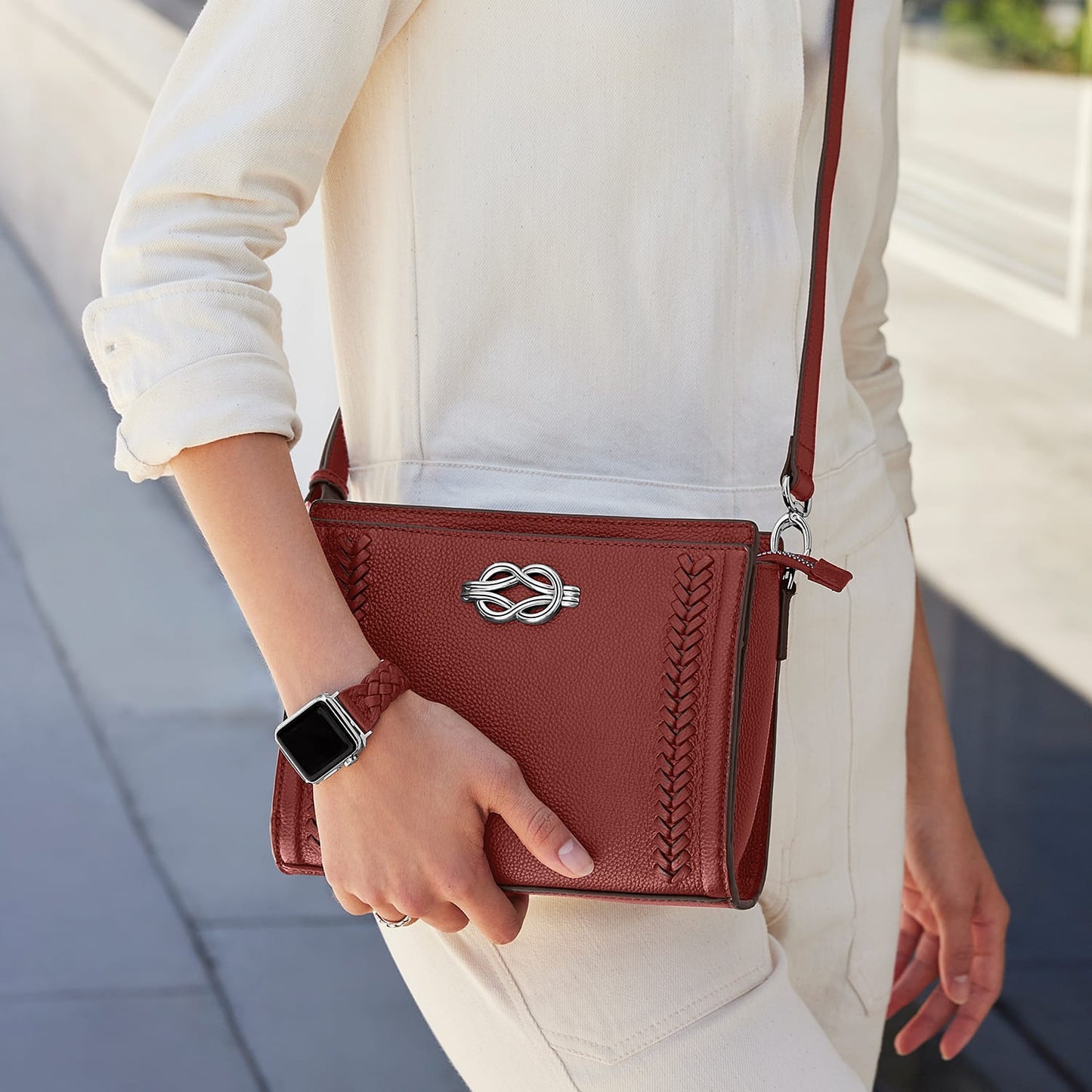 Model with a Brighton red leather crossbody handbag with silver knot accent and braided trim details