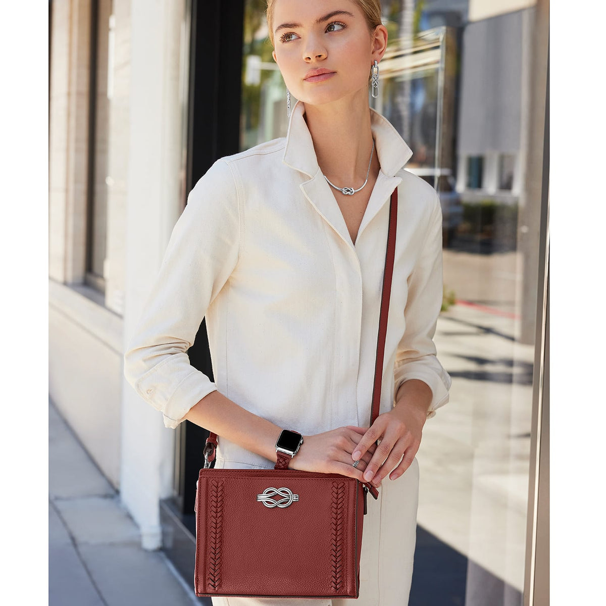 Model with a Brighton dark red leather crossbody handbag featuring silver knot clasp and braided trim details