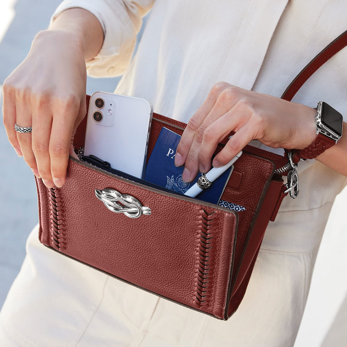 Model with a Brighton red leather handbag with silver-tone clasp and braided stitching, holding phone and passport