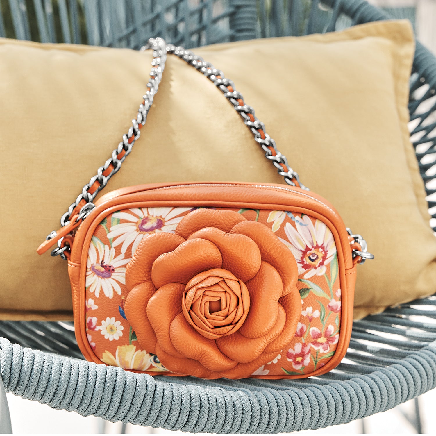 Brighton handbag with orange leather rosette and floral print, styled with a cushion on a woven chair