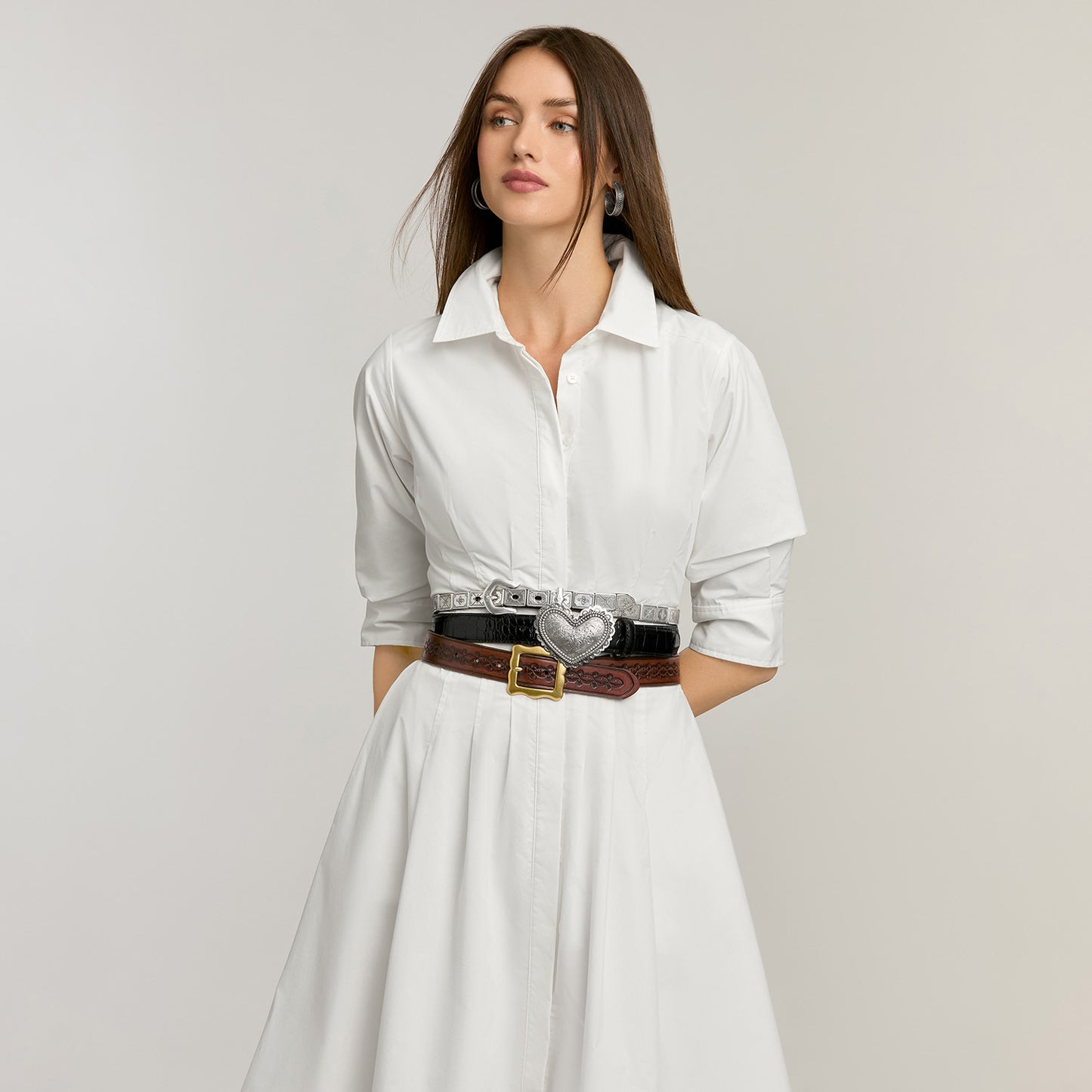 Model wearing Brighton leather belts stacked at the waist with silver studs, heart buckle, and brass buckle
