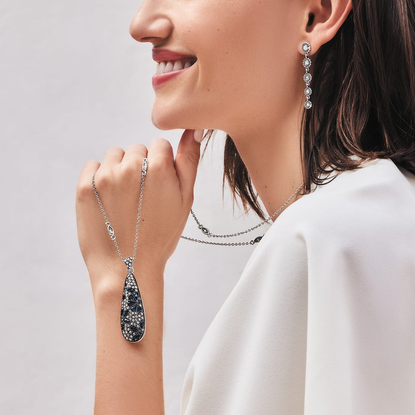 Model wearing a Brighton silver-plated crystal pendant necklace with blue teardrop pendant and coordinating Brighton accessories
