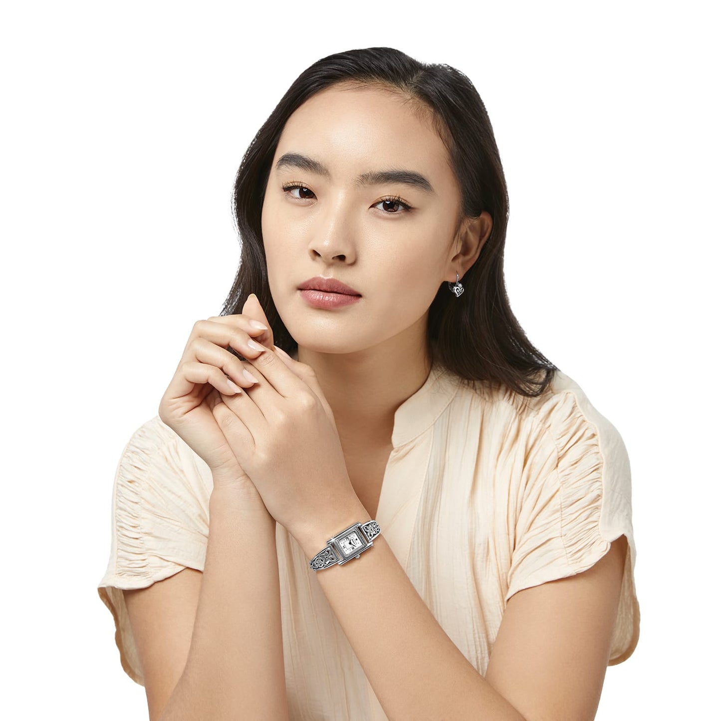 Model wearing a Brighton silver-plated watch with rectangular dial and scrollwork bracelet, paired with heart drop earrings