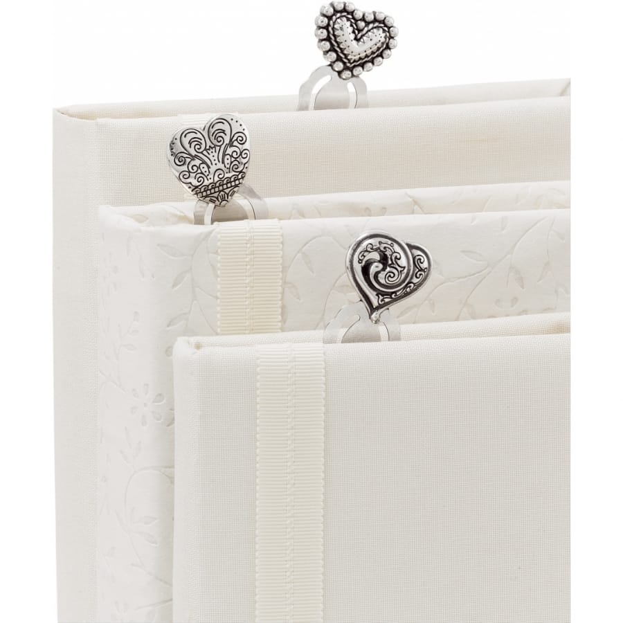 Brighton bookmarks with silver-plated heart-shaped charms in ornate scroll designs resting on ivory fabric books on a white background