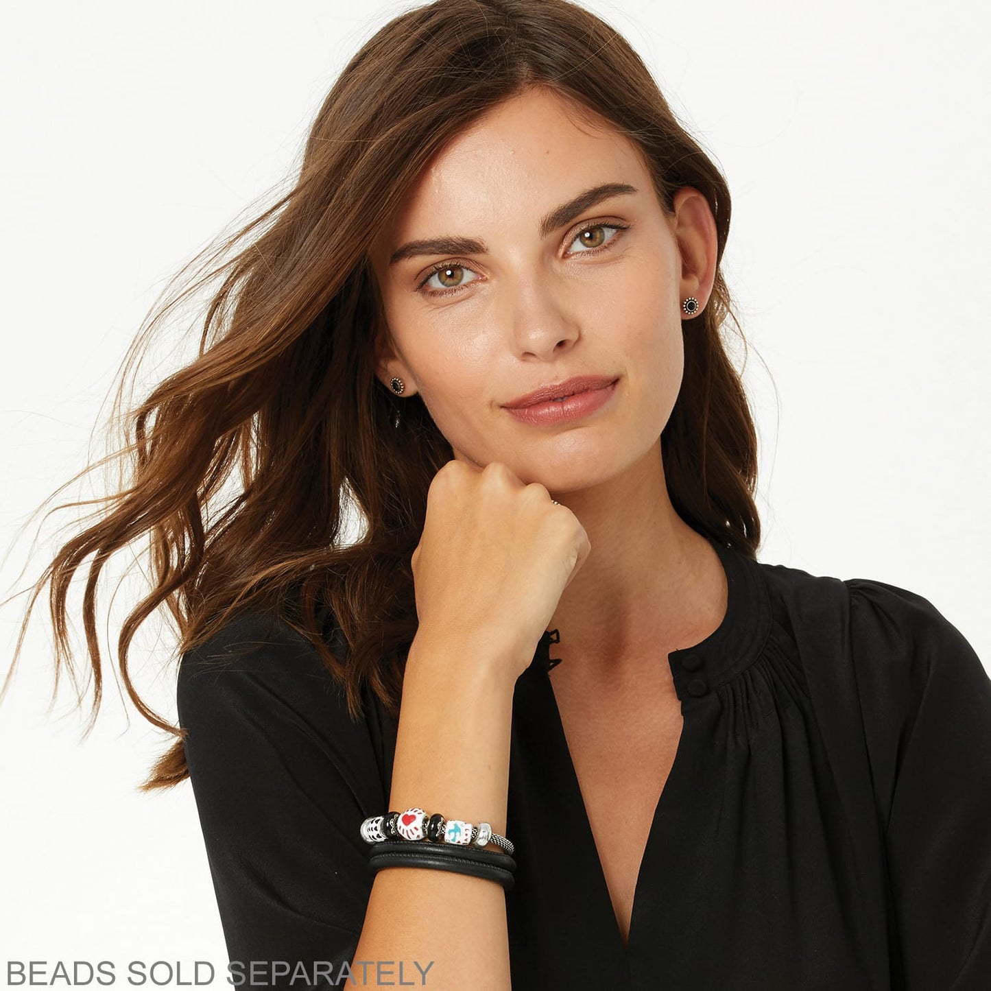 Model wearing stacked Brighton black leather bracelets with silver-plated charms and colorful decorative beads on wrist