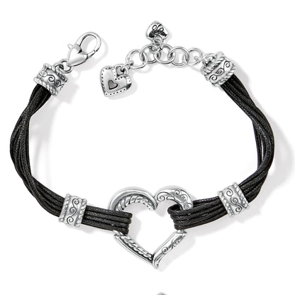 Brighton bracelet with black cord strands, silver-plated heart centerpiece, scroll accents, and heart charm on a white background