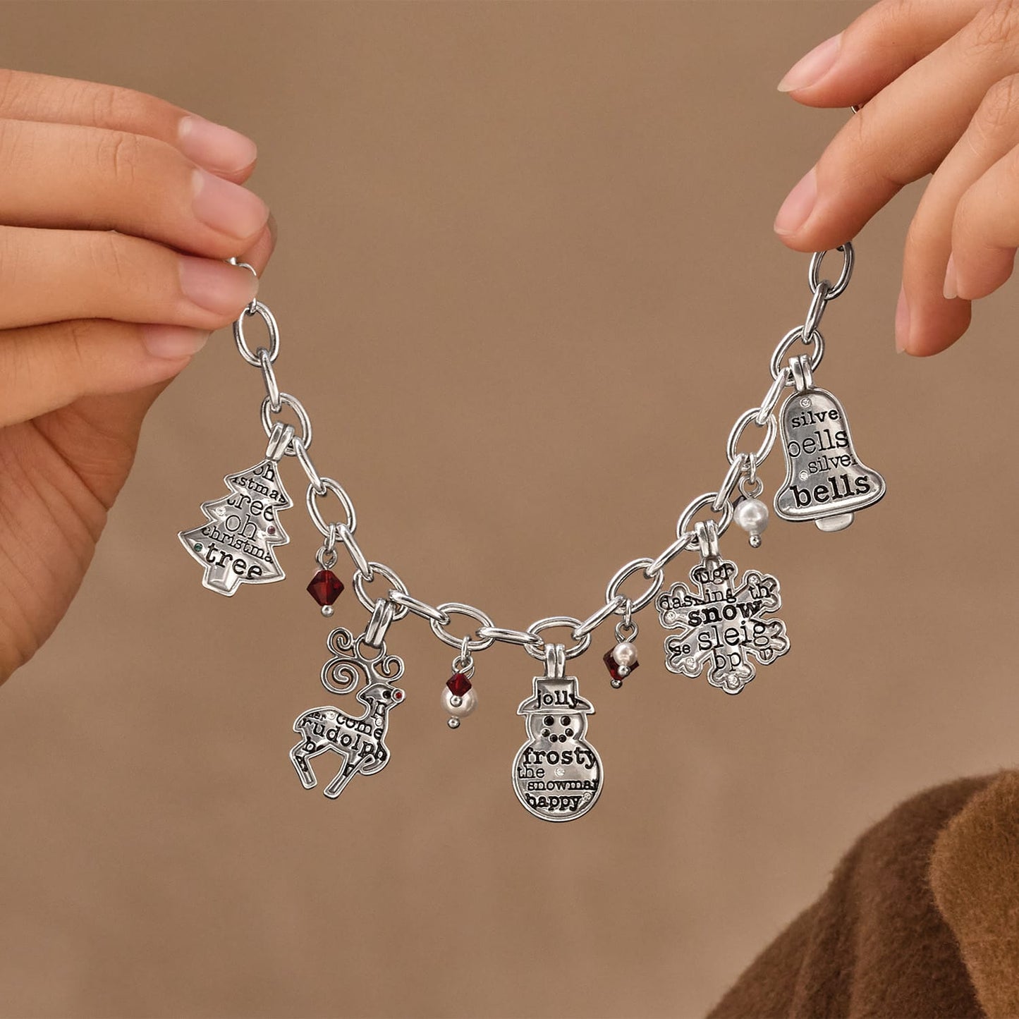 Model holding a Brighton silver-plated charm necklace with Christmas-themed charms, red crystals, and glass pearl beads