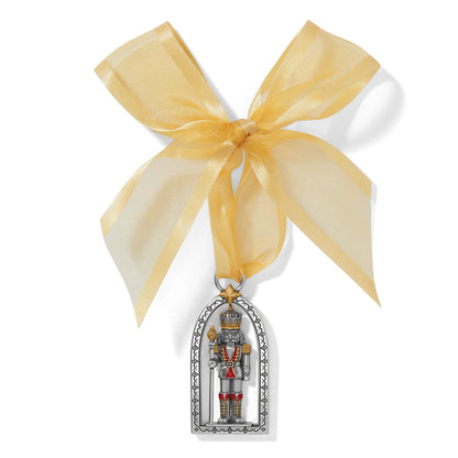 Brighton nutcracker ornament with two-tone finish and red accents, hung from a gold ribbon bow on a white background
