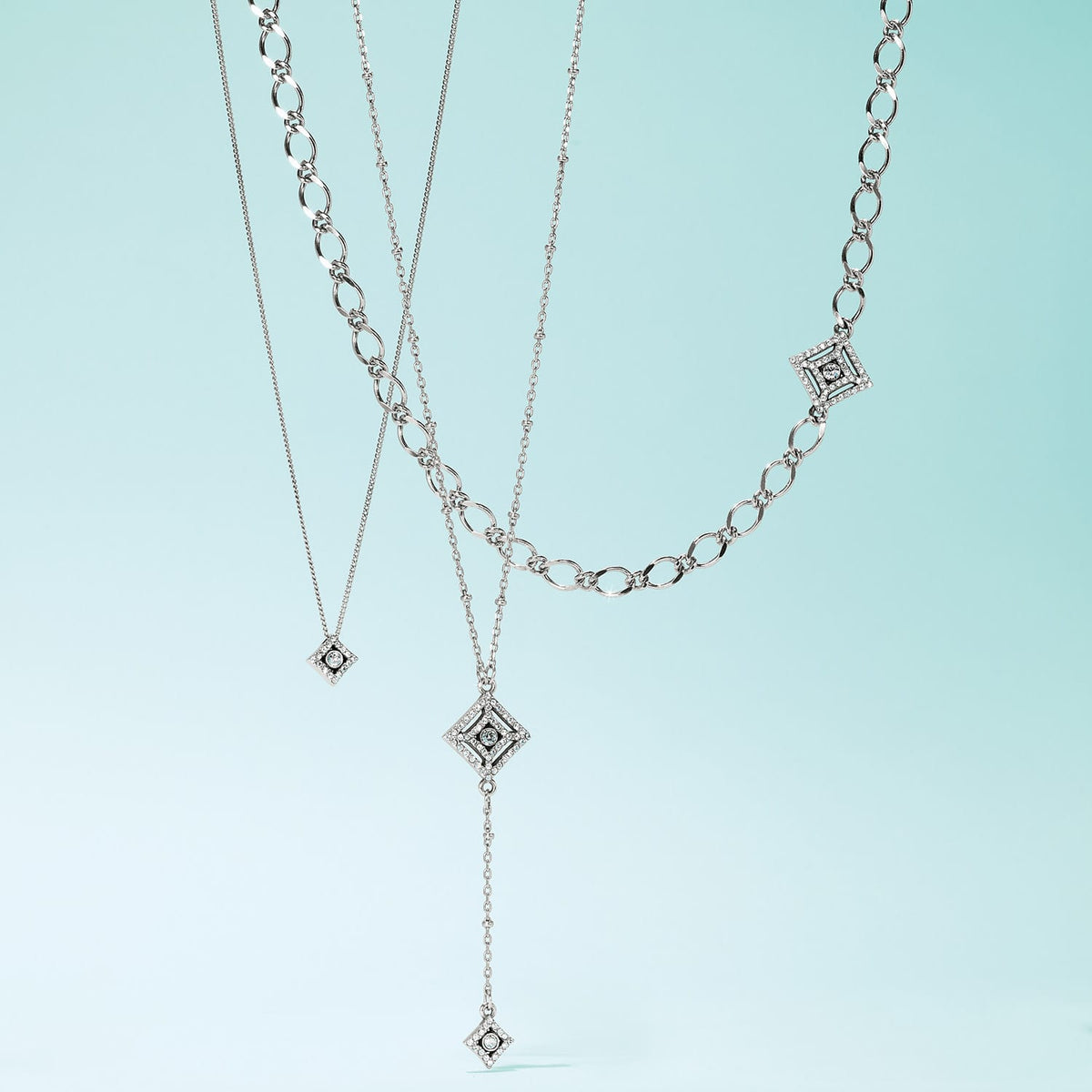 Brighton layered necklaces with silver-plated diamond-shaped pendants featuring crystal accents and varied chain styles on a white background