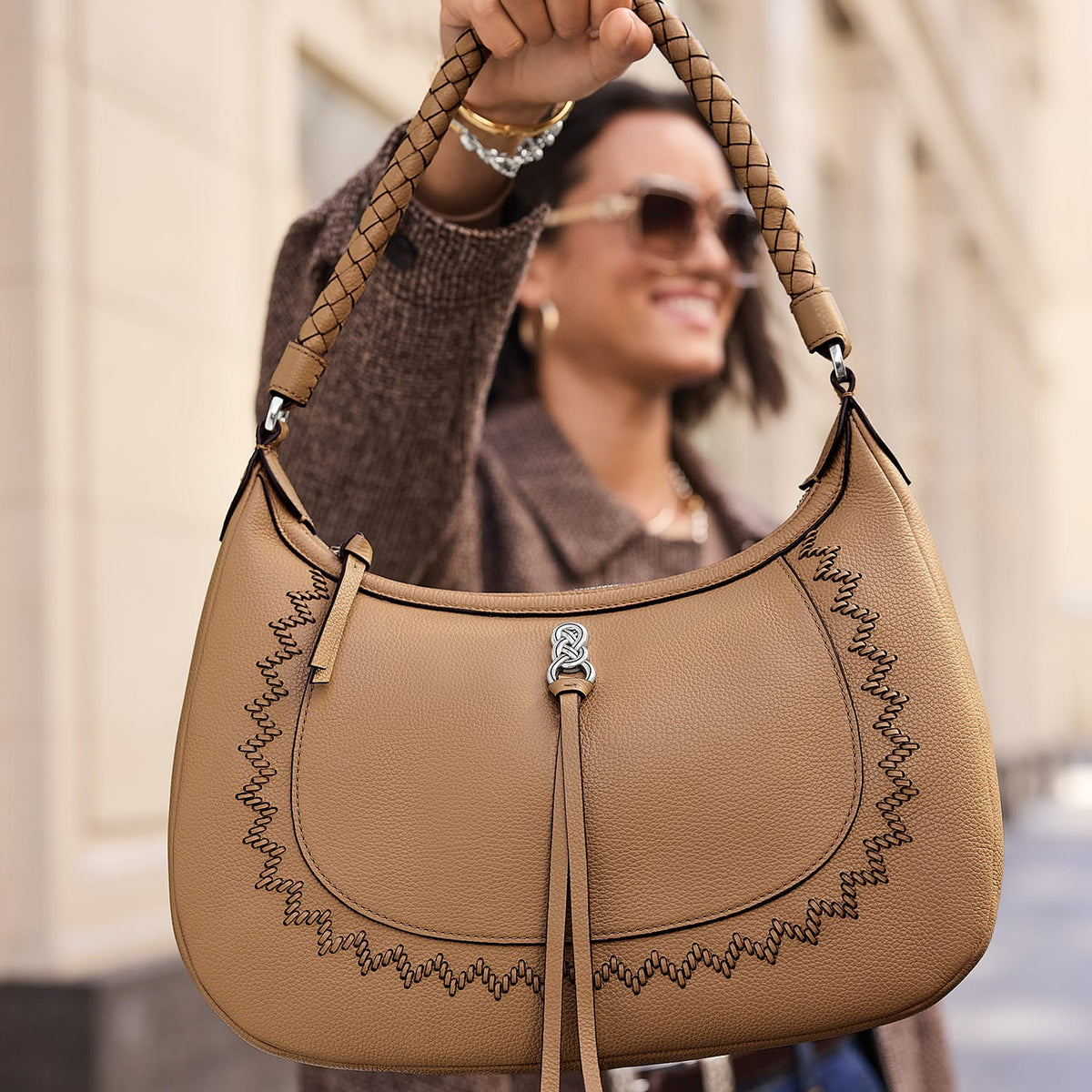 Model with a Brighton tan leather hobo handbag featuring braided strap, whipstitch trim, and silver-tone knot accent