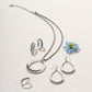 Brighton silver-plated jewelry set styled with a blue flower and coordinating pieces on a neutral woven background