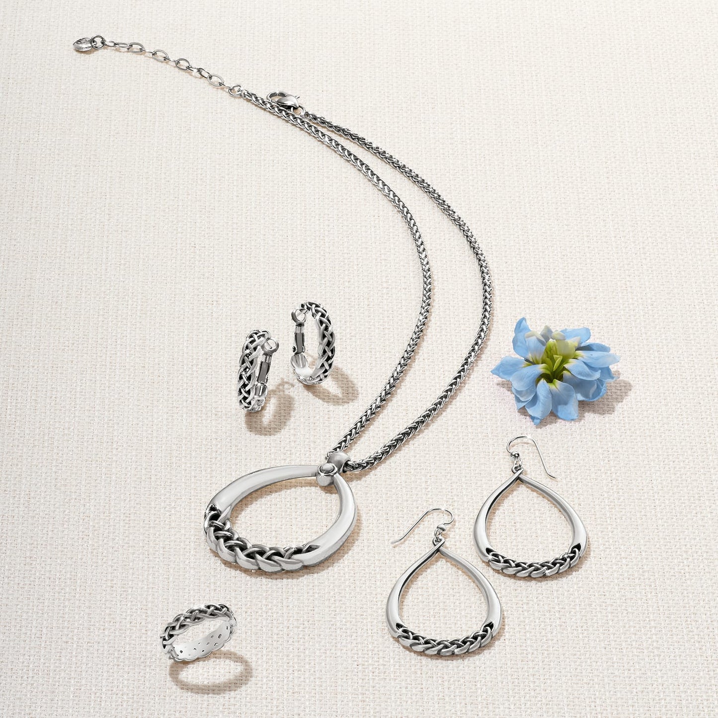 Brighton silver-plated jewelry set styled with a blue flower, featuring braided pendant necklace, teardrop earrings, hoops, and ring
