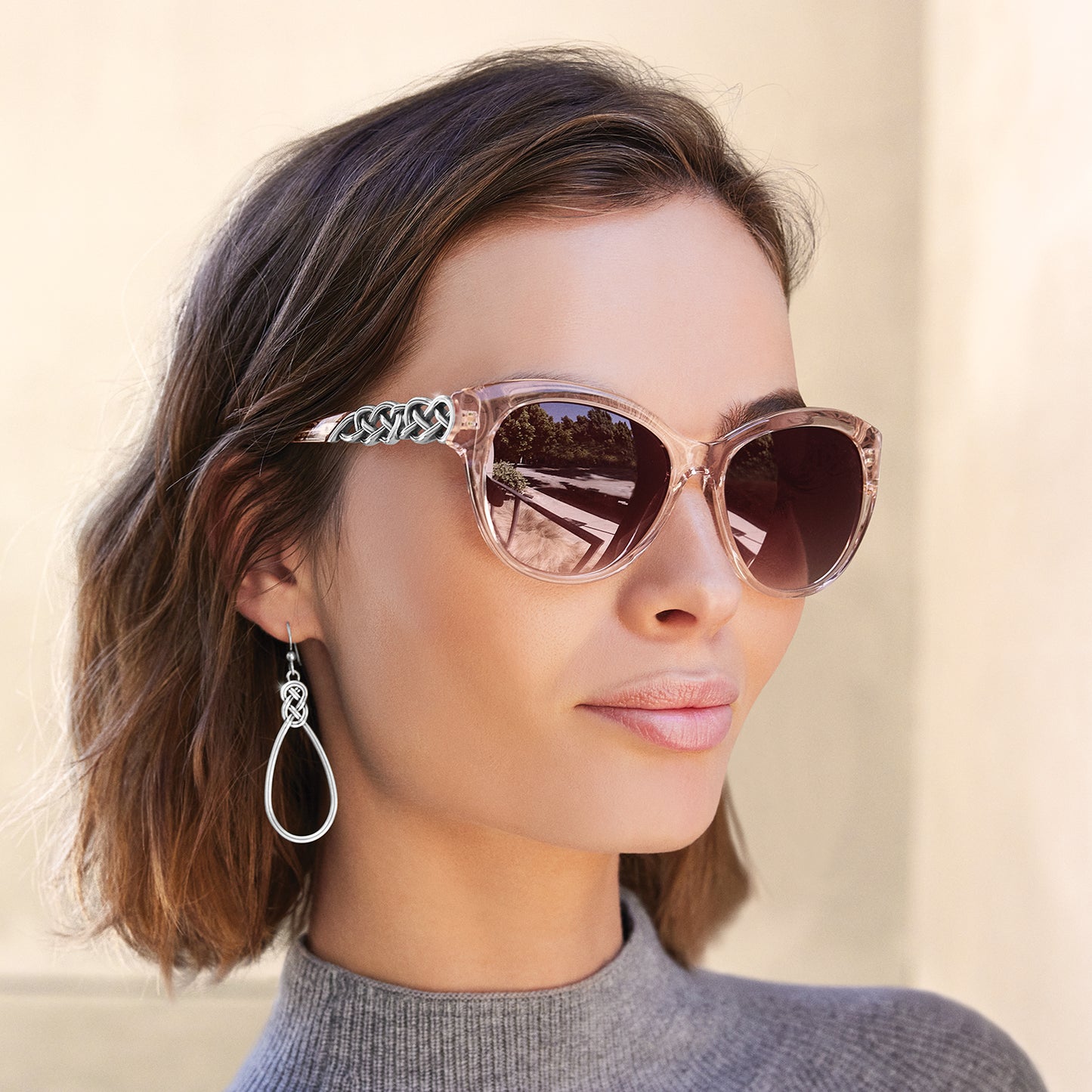 Model wearing Brighton pink cat-eye sunglasses with silver-tone Celtic knot temple detail, styled with Brighton teardrop earrings