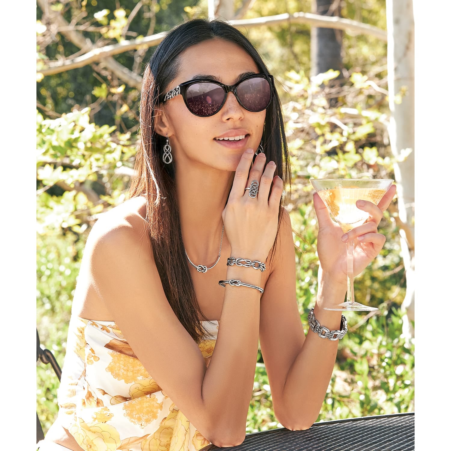 Model wearing Brighton silver-plated sunglasses with knot-detail temples and coordinating Brighton accessories including earrings, rings, and bracelets