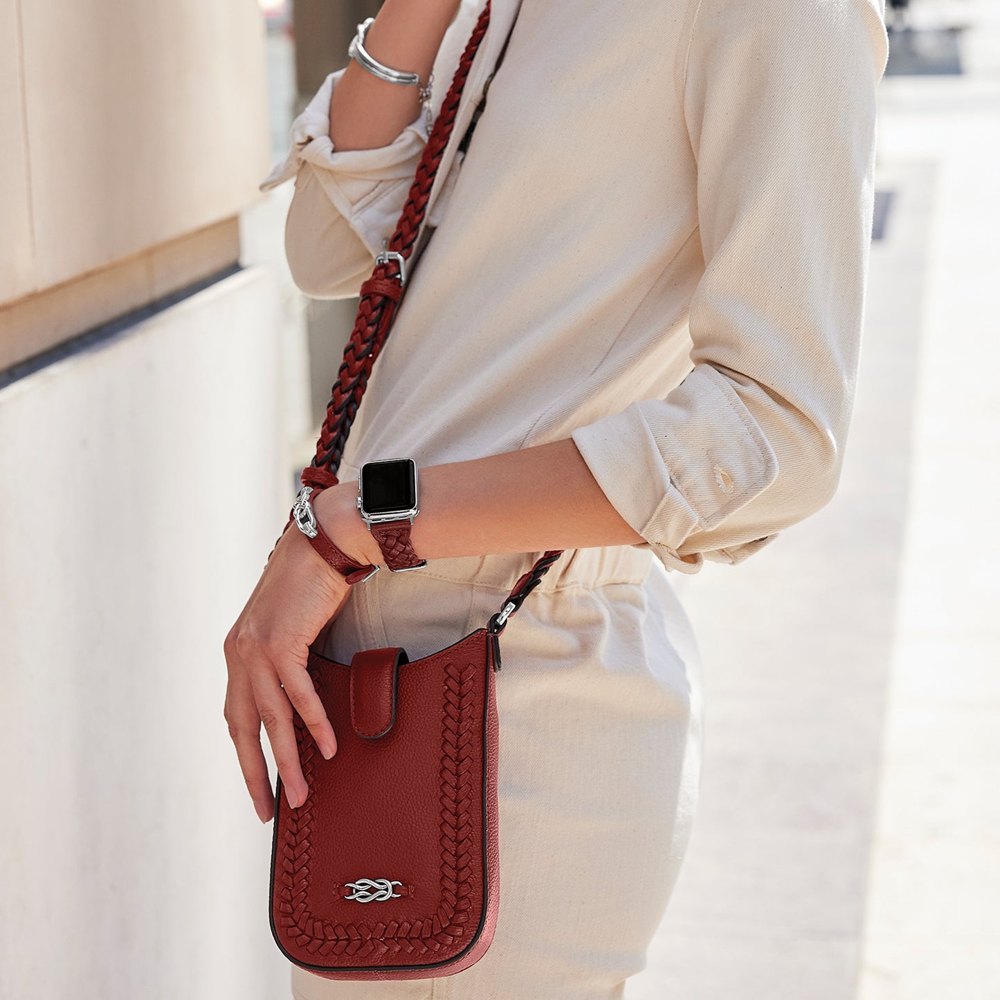 Model with a Brighton red leather crossbody bag featuring braided trim, knot detail, and braided shoulder strap