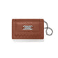 Brighton brown leather wallet with silver-tone interlocking knot emblem, woven trim, and chain wristlet on a white background