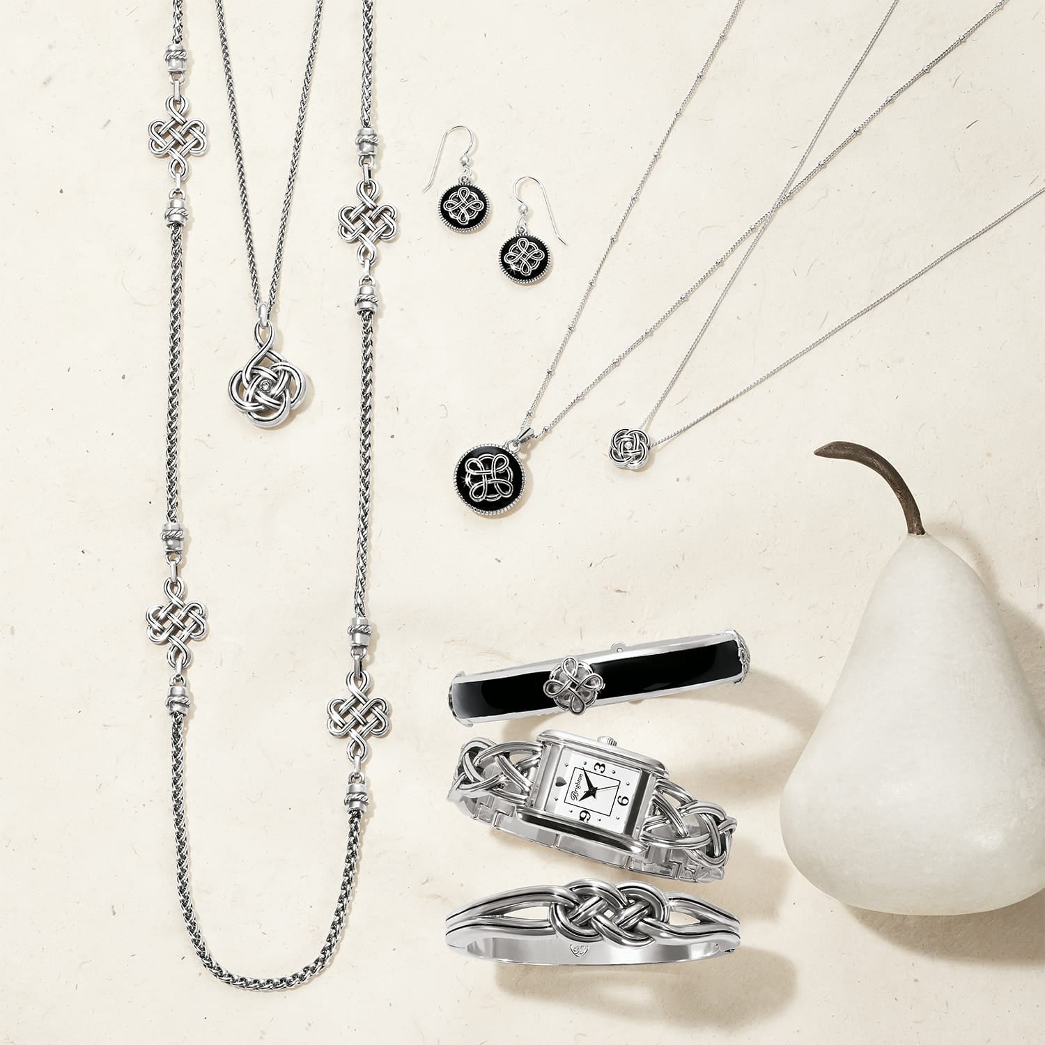 Brighton silver-plated jewelry collection styled with a white pear and Celtic knot accents on a neutral background