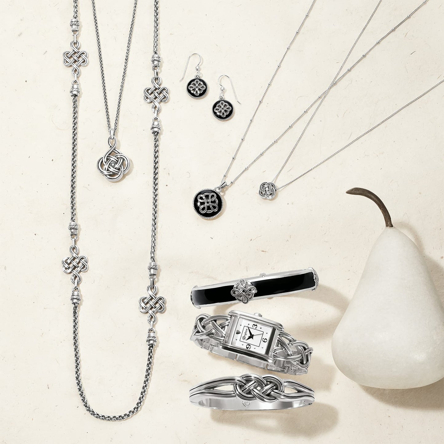 Brighton silver-plated jewelry collection styled with a white pear and Celtic knot accents on a neutral background