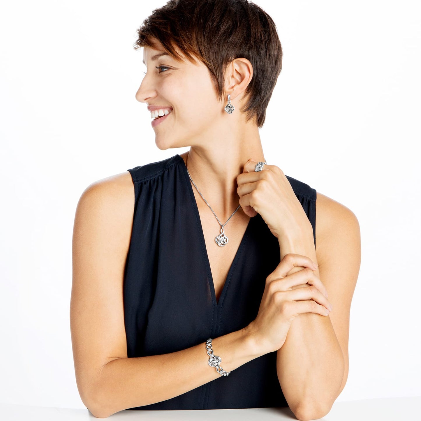 Model wearing a Brighton silver-plated knot pendant necklace with coordinating Brighton earrings, ring, and bracelet accessories