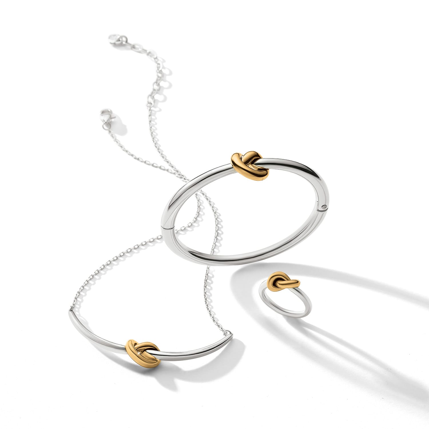 Brighton two-tone jewelry set styled with silver bangle, necklace, and ring featuring gold knot accents on white background