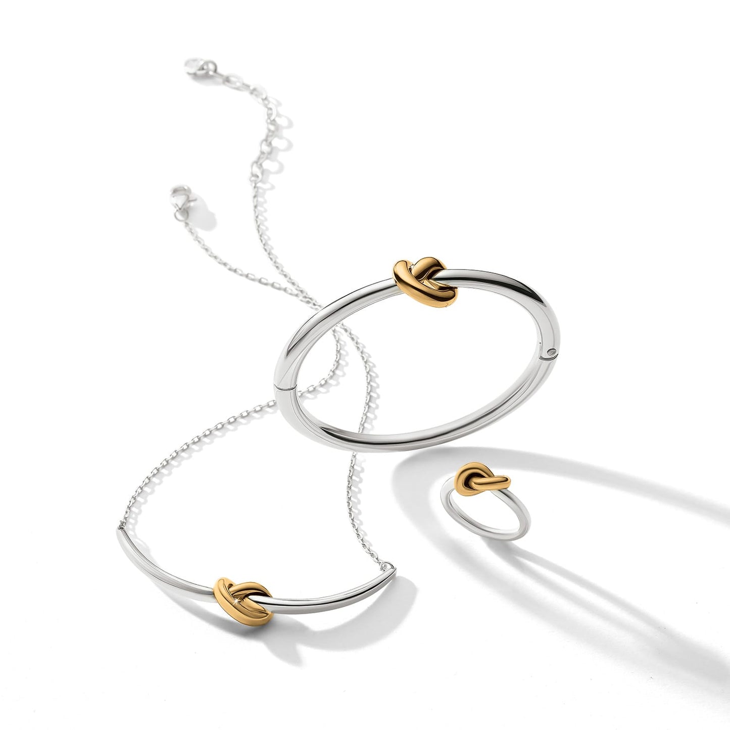 Brighton two-tone jewelry set styled with silver bangle, necklace, and ring featuring gold knot accents on white background