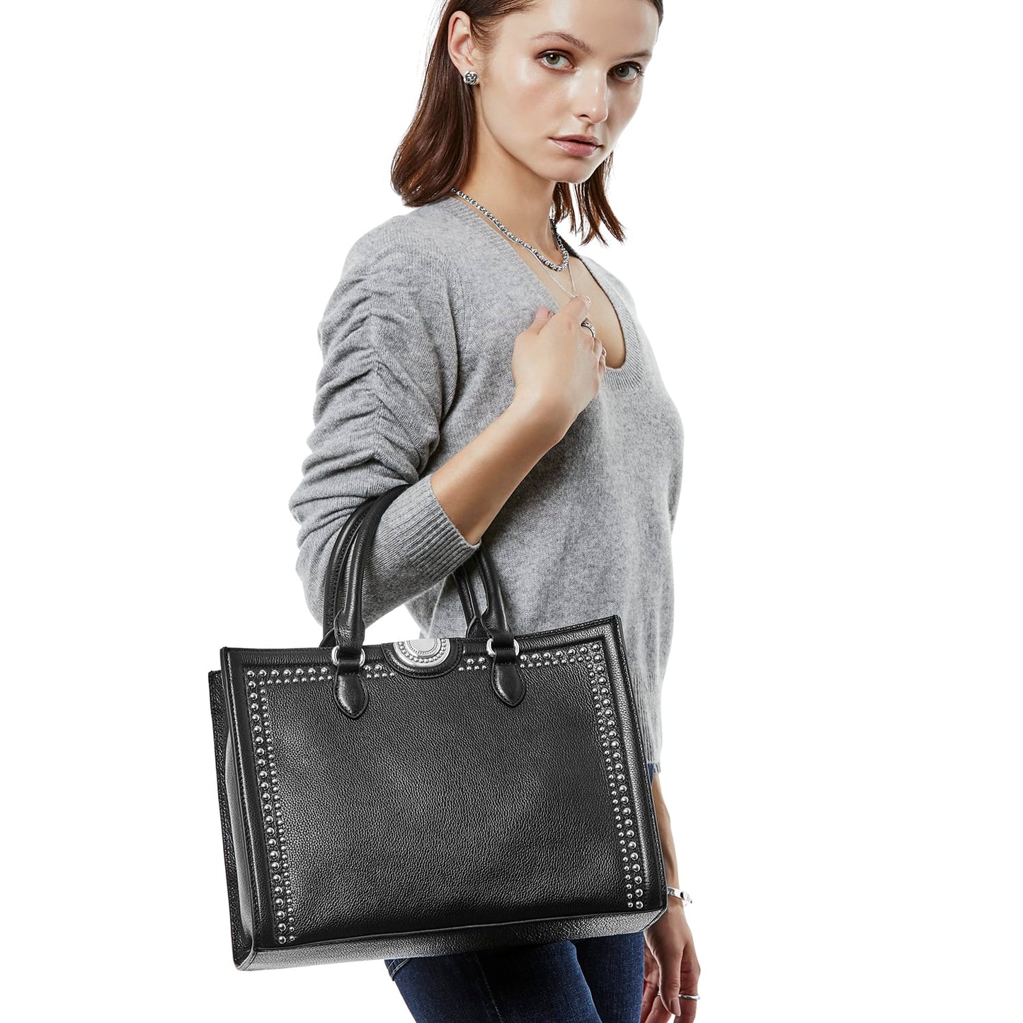 Model with a Brighton black leather tote handbag featuring silver-tone studded trim and circular medallion accent