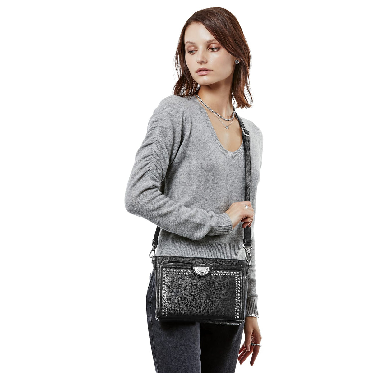 Model with a Brighton black leather crossbody handbag featuring silver-tone stud trim and medallion accent