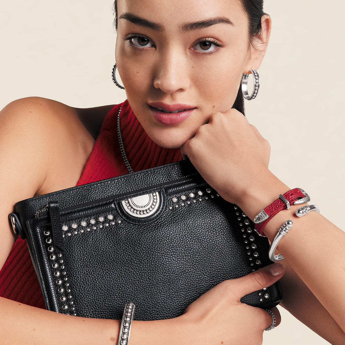 Brighton black studded handbag with silver-tone medallion, held by model wearing coordinating Brighton silver hoop earrings and bracelets