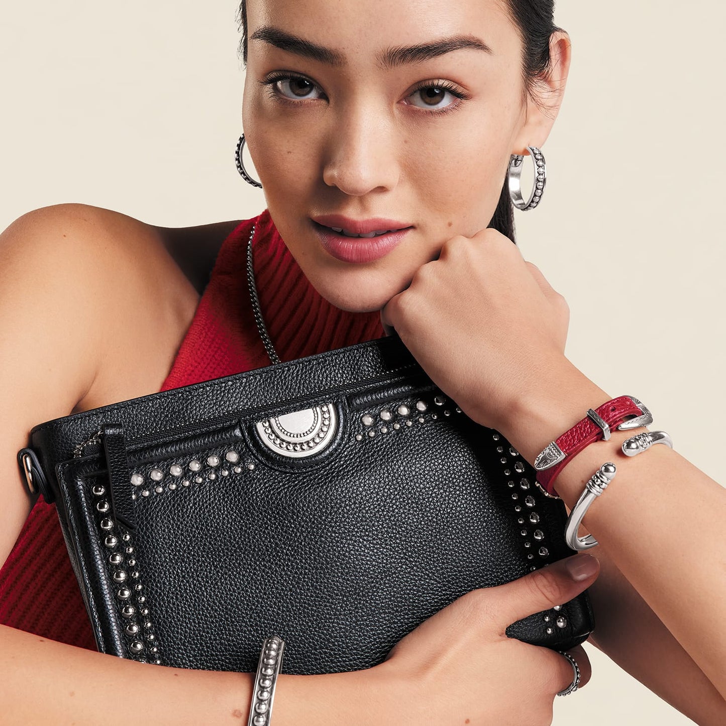 Brighton black studded handbag with silver-tone medallion, held by model wearing coordinating Brighton silver hoop earrings and bracelets
