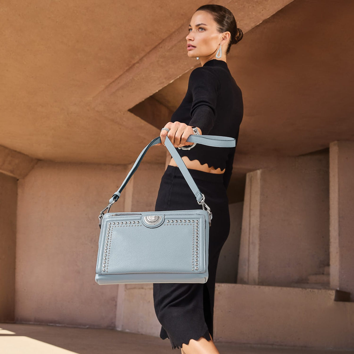 Model with a Brighton light blue leather handbag featuring silver-tone studded trim and circular medallion accent