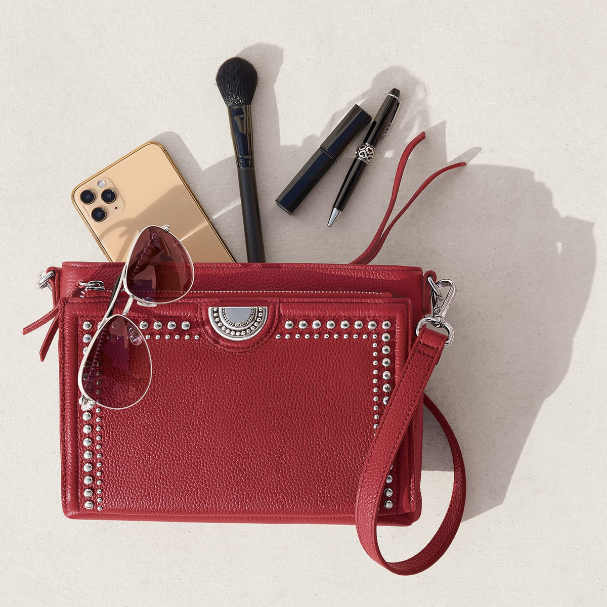 Brighton red studded leather handbag styled with sunglasses and other accessories on a neutral background