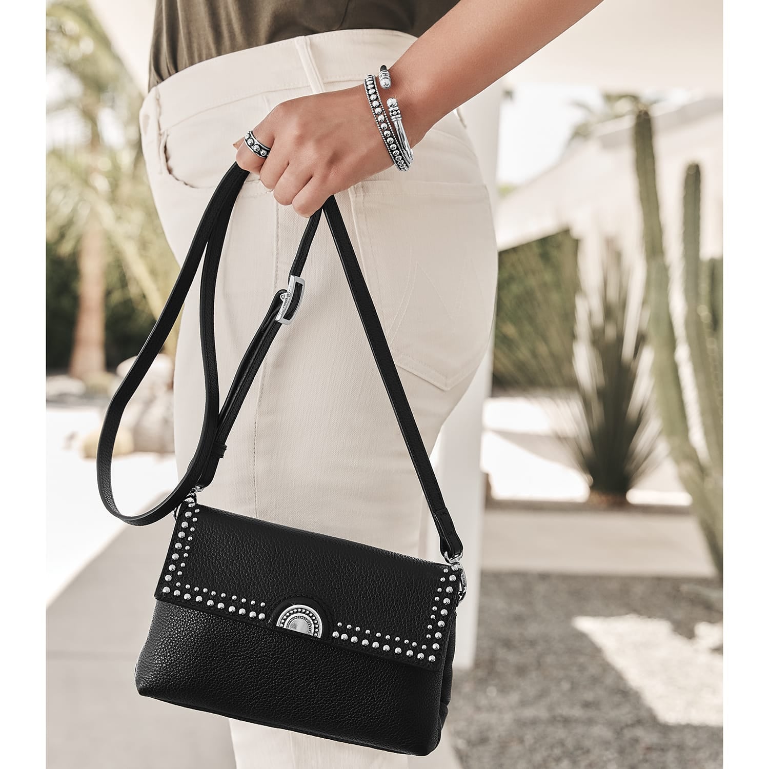 Model with a Brighton black leather handbag with silver-tone studded trim and round medallion clasp