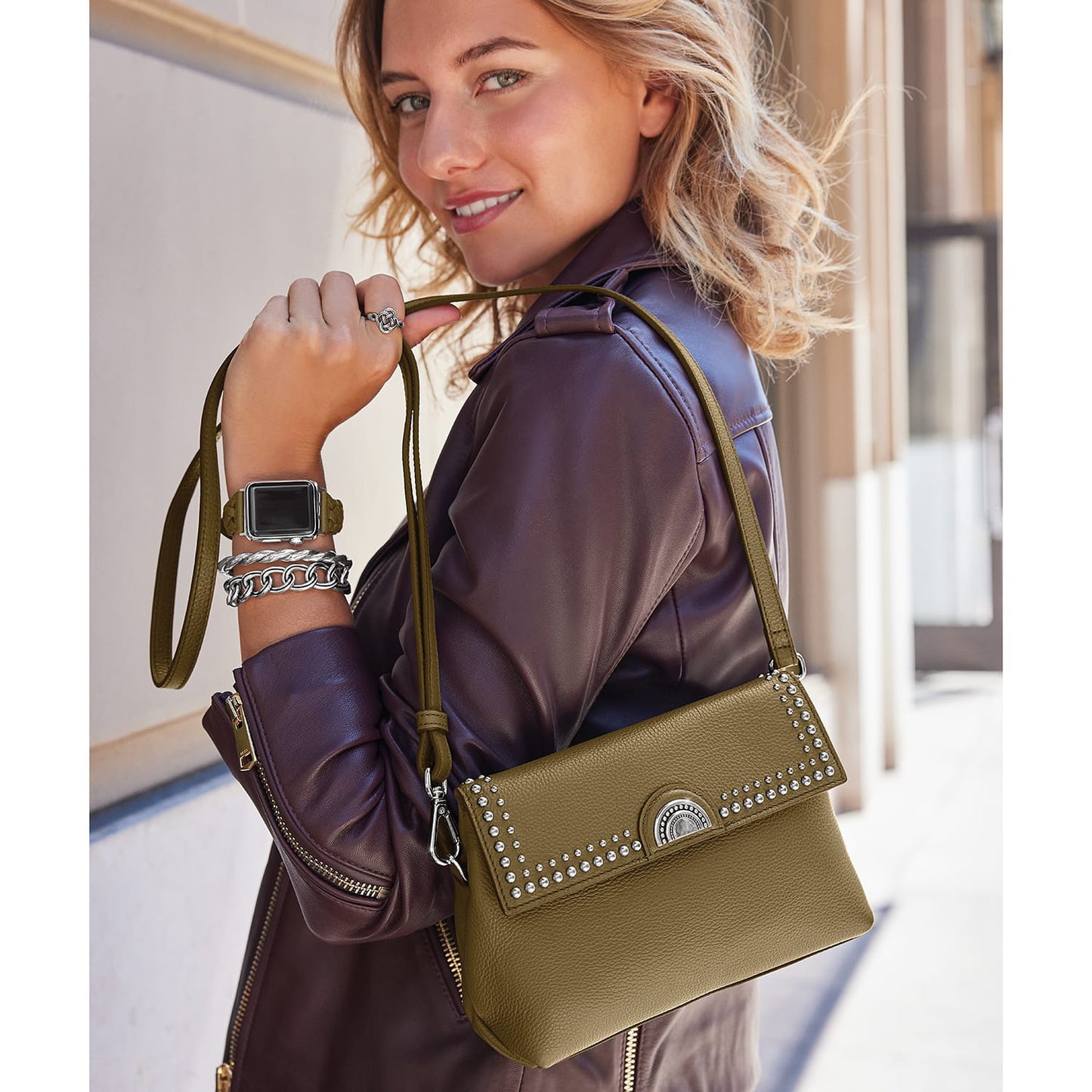 Model with a Brighton olive green shoulder handbag featuring silver studded trim and round medallion clasp