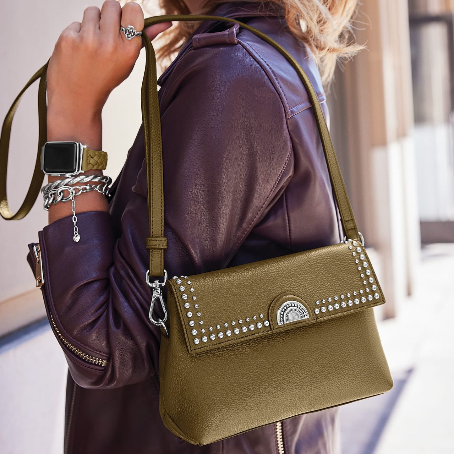 Model with a Brighton olive green leather handbag featuring crystal stud trim and silver-tone medallion accent