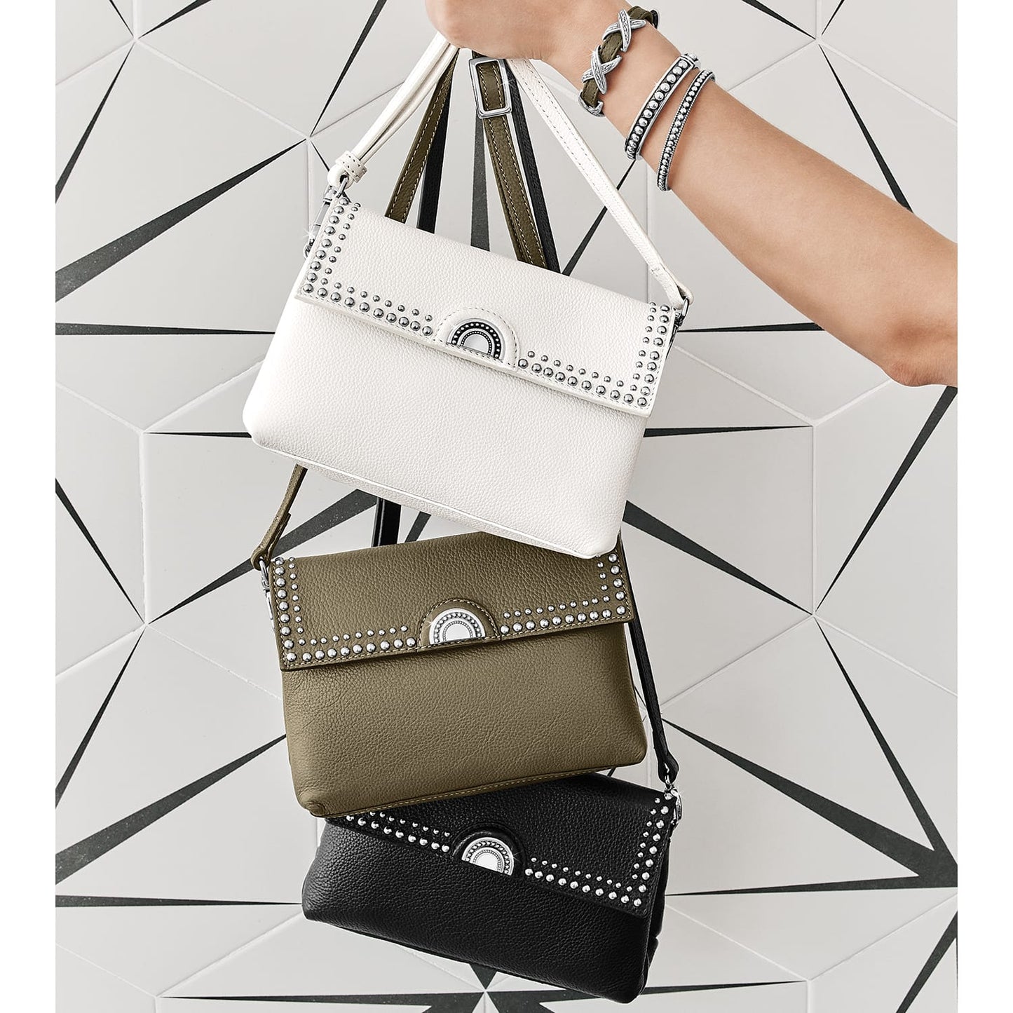 Model with three Brighton studded leather handbags in white, olive, and black with silver-tone hardware accents