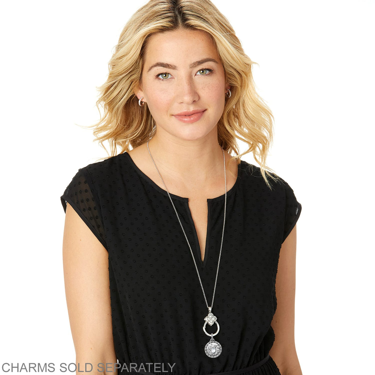 Model wearing a Brighton silver-plated long pendant necklace with floral medallion and round engraved charm.
