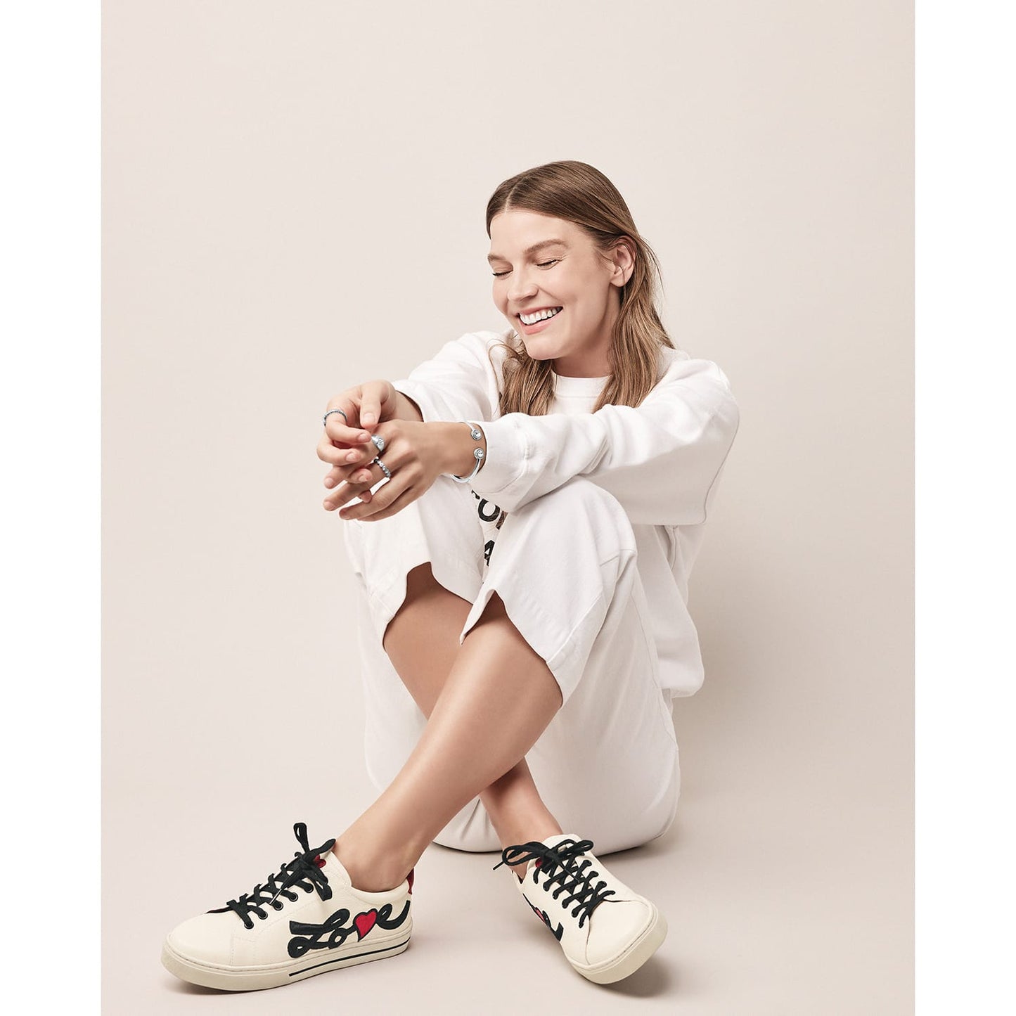 Model wearing Brighton ivory leather sneakers with black laces, red heart accents, and Love script embroidery