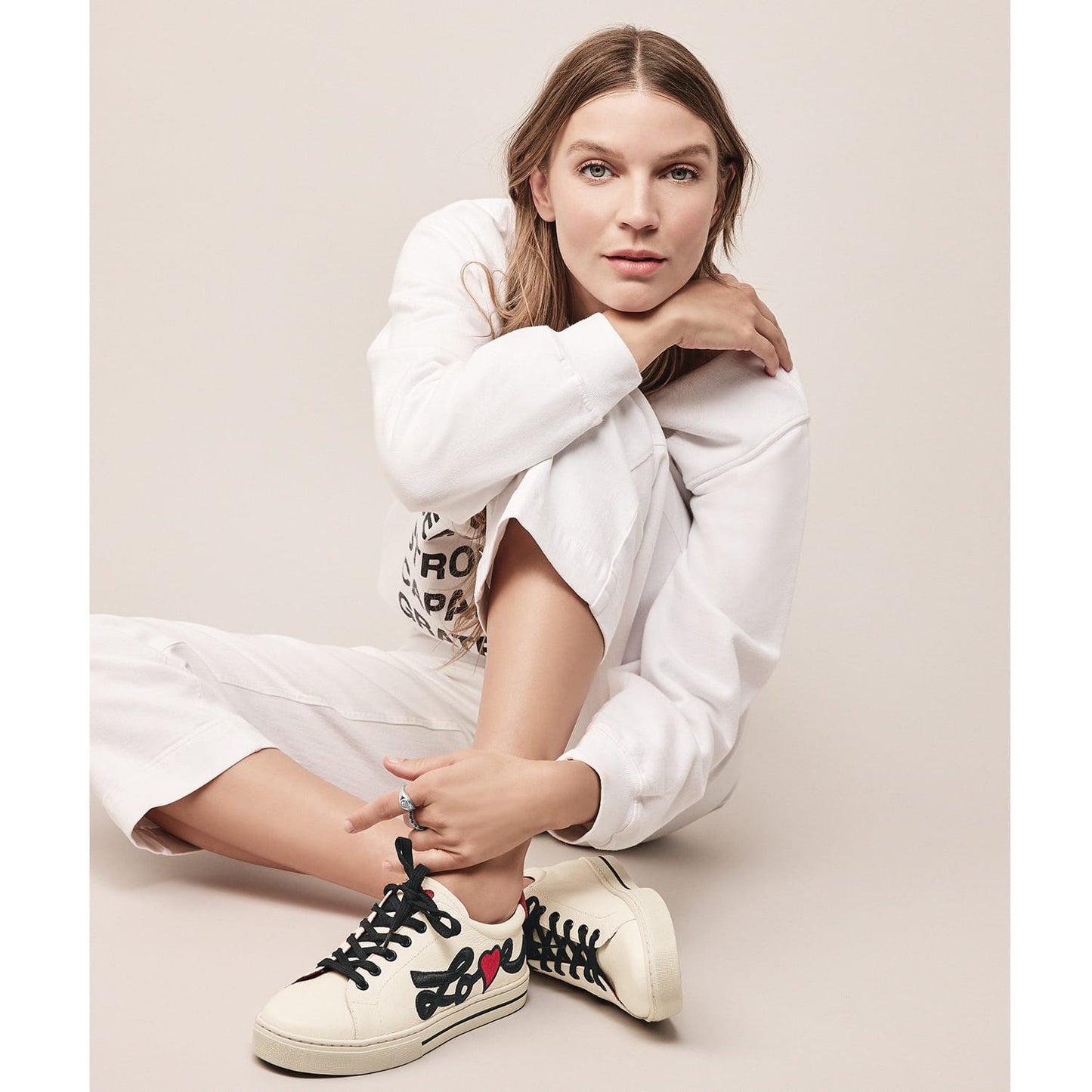 Model wearing Brighton leather sneakers in cream with black Love script embroidery, red heart accent, and black laces