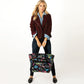 Model with a Brighton black tote bag featuring colorful travel-themed graphic print and dual top handles