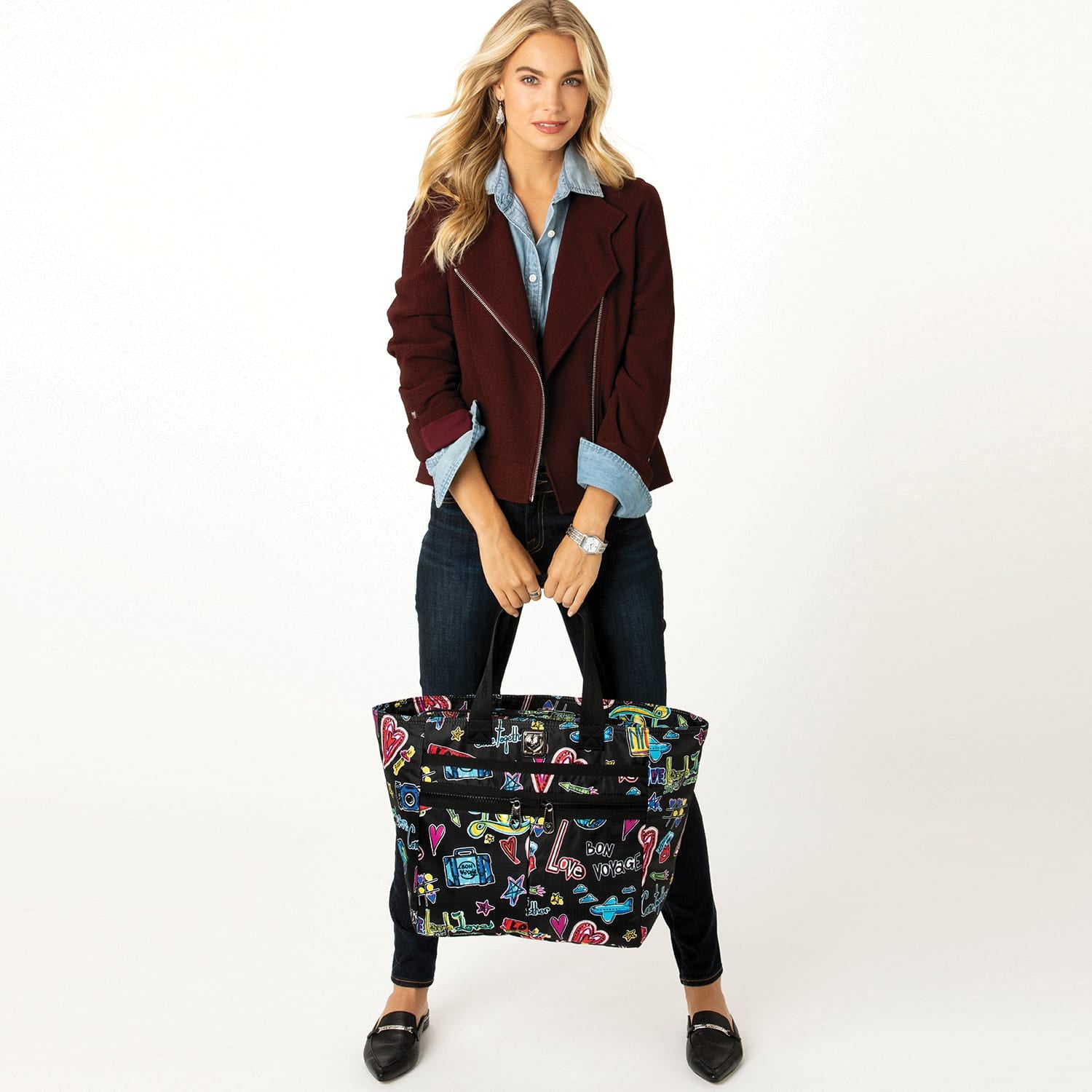 Model with a Brighton black tote bag featuring colorful travel-themed graphic print and dual top handles